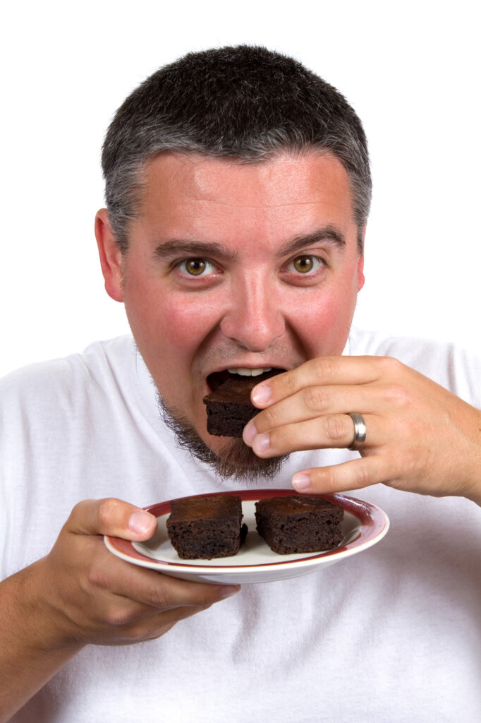 Man with beard eats homemade brownies while holding plate.